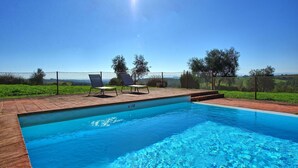 Una piscina rectangular con superficie de agua azul cristalina, rodeada por un deck de ladrillo. Hay dos sillones de descanso y una mesita en el deck.