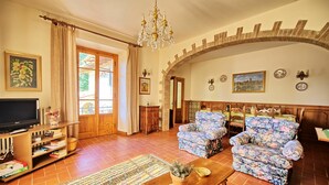 A living room with a television, floral armchairs, a coffee table, and a chandelier. - Casale Ambra - Country house with private pool (Ambra)