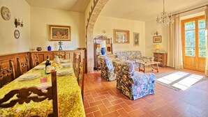 A dining area with a long table set for a meal, a sofa, and a chandelier. - Casale Ambra - Country house with private pool (Ambra)