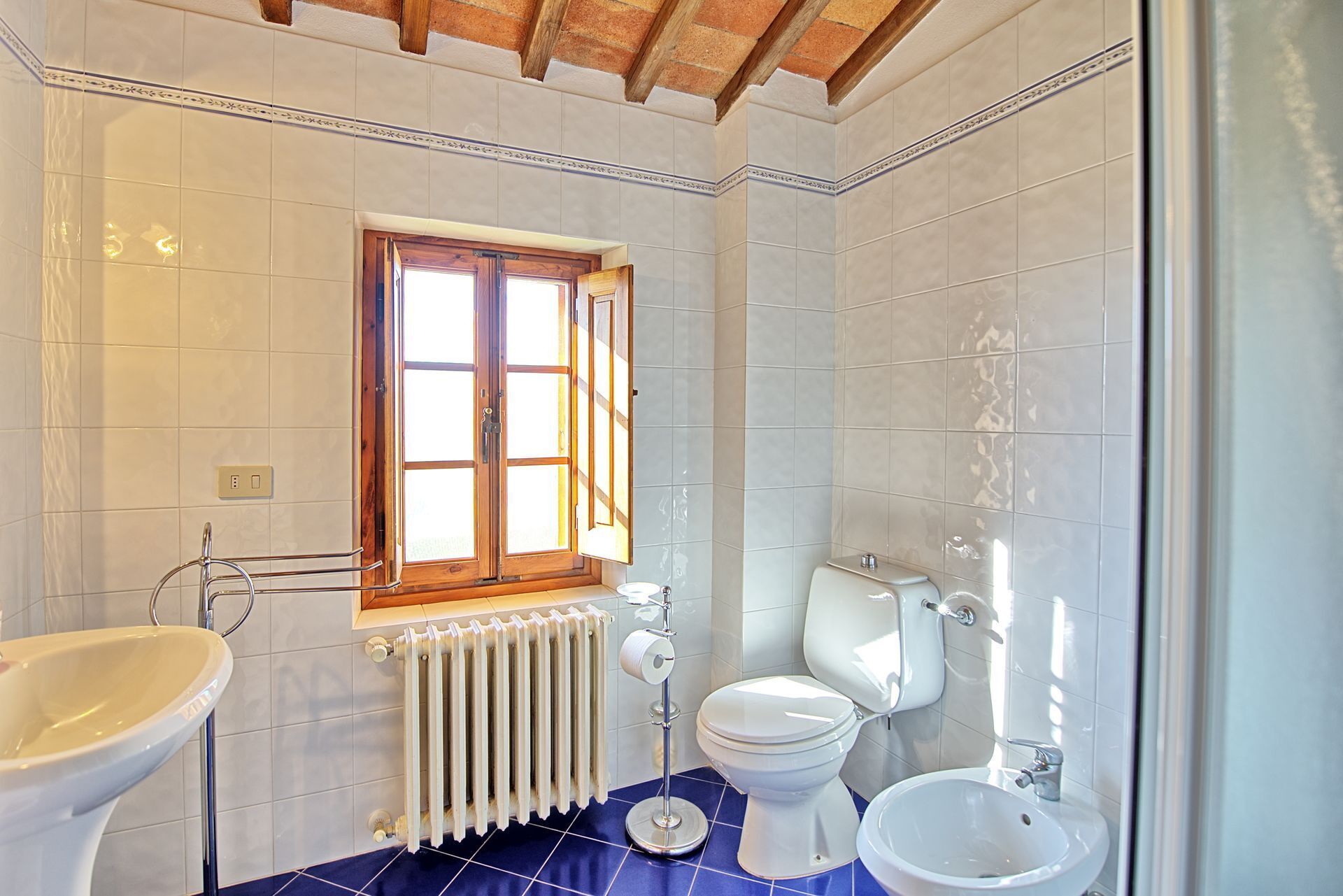 Un baño con ventana, radiador, inodoro, bidé y lavamanos.