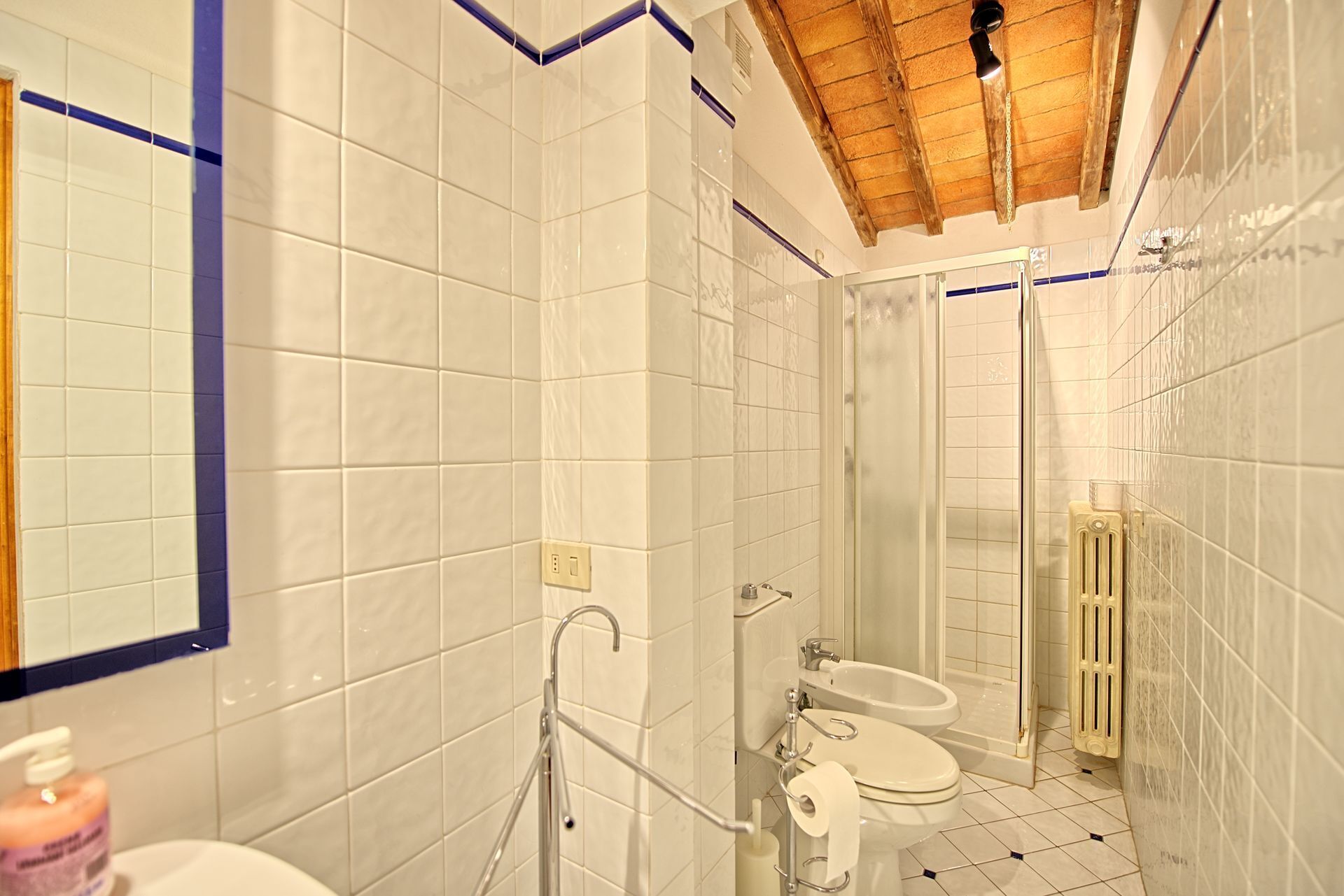 Ein Badezimmer mit weißen Fliesen, Holzboden und einer Dusche, Toilette und einem Waschbecken.