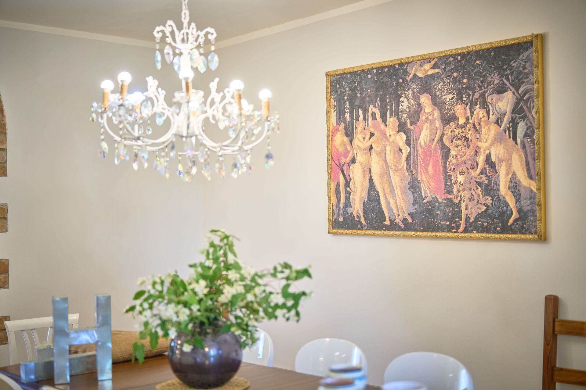 A dining area with a chandelier, a table with chairs, and a framed painting on the wall.
