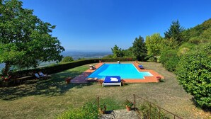 Ein rechteckiger Swimmingpool mit blauer Abdeckung, umgeben von einer Rasenfläche mit Liegestühlen und Topfpflanzen.