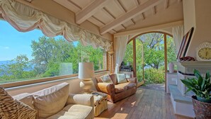 Ein sonnendurchfluteter Raum mit Holzbalkendecke, einer Couch, einem Tisch und Blick auf Grünflächen.