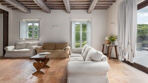 Amplia sala de estar con dos sofás, una mesa de centro de madera y ventanas grandes con vistas a zonas verdes.