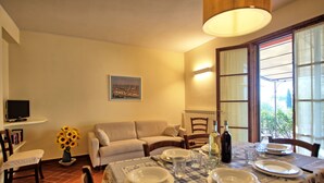 A dining area with a table set for four, a sofa, a television, and a window with a view. - Casa Rossa 4 - Apartment with swimming pool (Gorgognano)