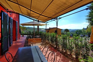 An outdoor patio with a table and chairs, a large umbrella, and a view of the countryside. - Casa Rossa 4 by PosarelliVillas (Gorgognano)