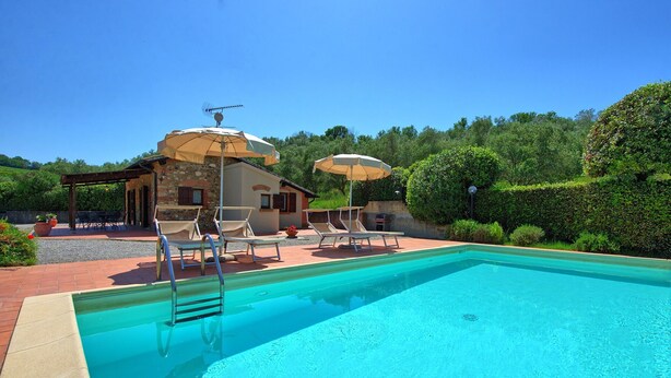 Ein Swimmingpool mit Liegestühlen und Sonnenschirmen, umgeben von einem Steinhaus mit Garten.