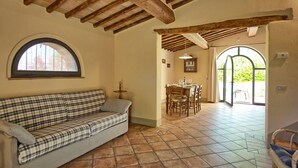 A cozy room with a checkered sofa, a dining table set for four, and a large arched doorway leading outside. - Glicini 2 - Apartment with swimming pool (Noce)