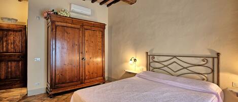 A bedroom with a wooden wardrobe, a bed with a metal headboard, and a wall-mounted lamp.