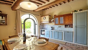 A kitchen with wooden cabinets, a dining table set for four, and a large window providing natural light. - Glicini 2 - Apartment with swimming pool (Noce)