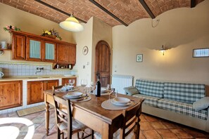 A cozy kitchen with wooden cabinets, a dining table set for four, and a plaid sofa in the living area.
