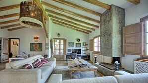 A spacious living room with a high ceiling and exposed wooden beams, a fireplace, and a cozy seating area with a sofa and coffee table.