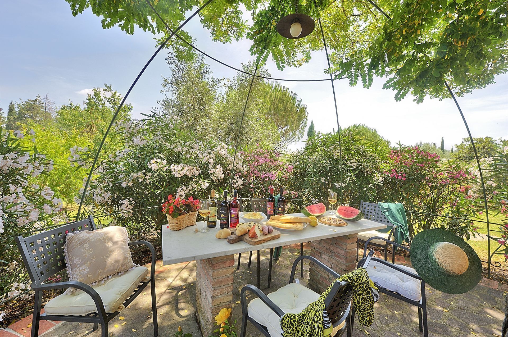 Un espace de restauration en plein air avec une table dressée pour un repas, entourée de chaises et agrémentée d’un panier de fleurs.