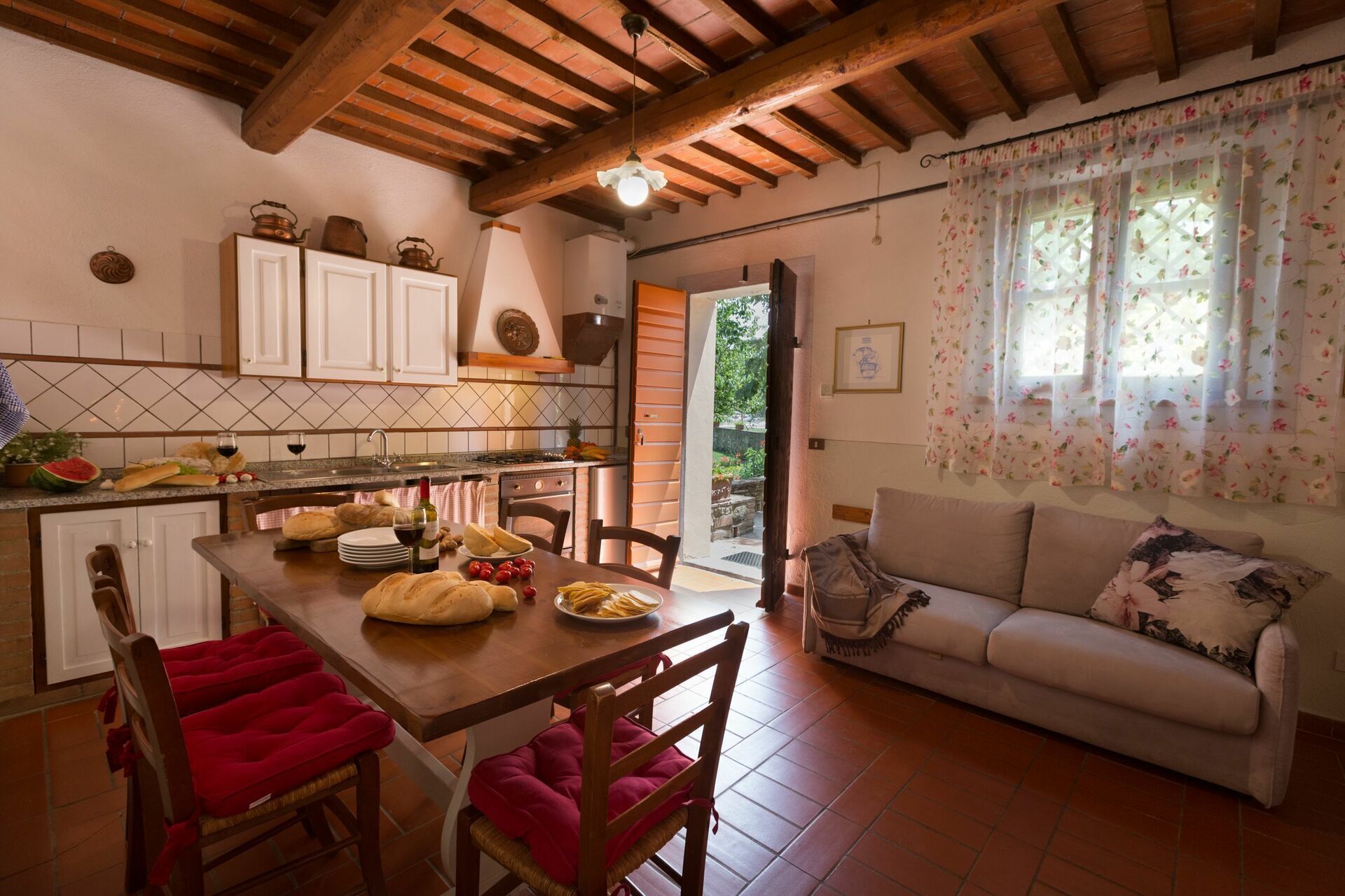Una cuina acollidora amb bigues de fusta, una taula de menjador preparada amb pa i plats, i un sofà a la zona de sala d'estar.