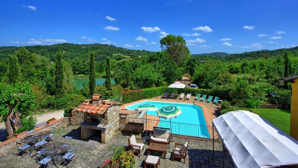 Un área de piscina con sillones de descanso y sombrillas, rodeada de exuberante vegetación y colinas.