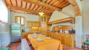 Una cocina rústica con armarios de madera, una larga mesa de comedor para seis personas y una estufa empotrada.