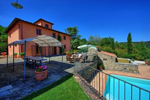 A villa with a swimming pool, outdoor seating, and a stone structure.