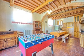 A cozy room with a foosball table, wooden cabinets, a dining table, and a kitchen area.