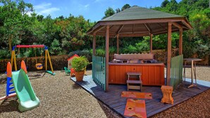 Una terraza de madera con un jacuzzi, un columpio y un área de juegos.