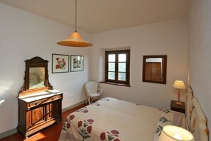 A bedroom with a bed, a dresser, a chair, a window, and a hanging lamp.