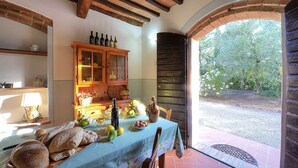 Un comedor rústico con una mesa dispuesta para una comida, un armario de madera con botellas y vistas al jardín a través de un arco.