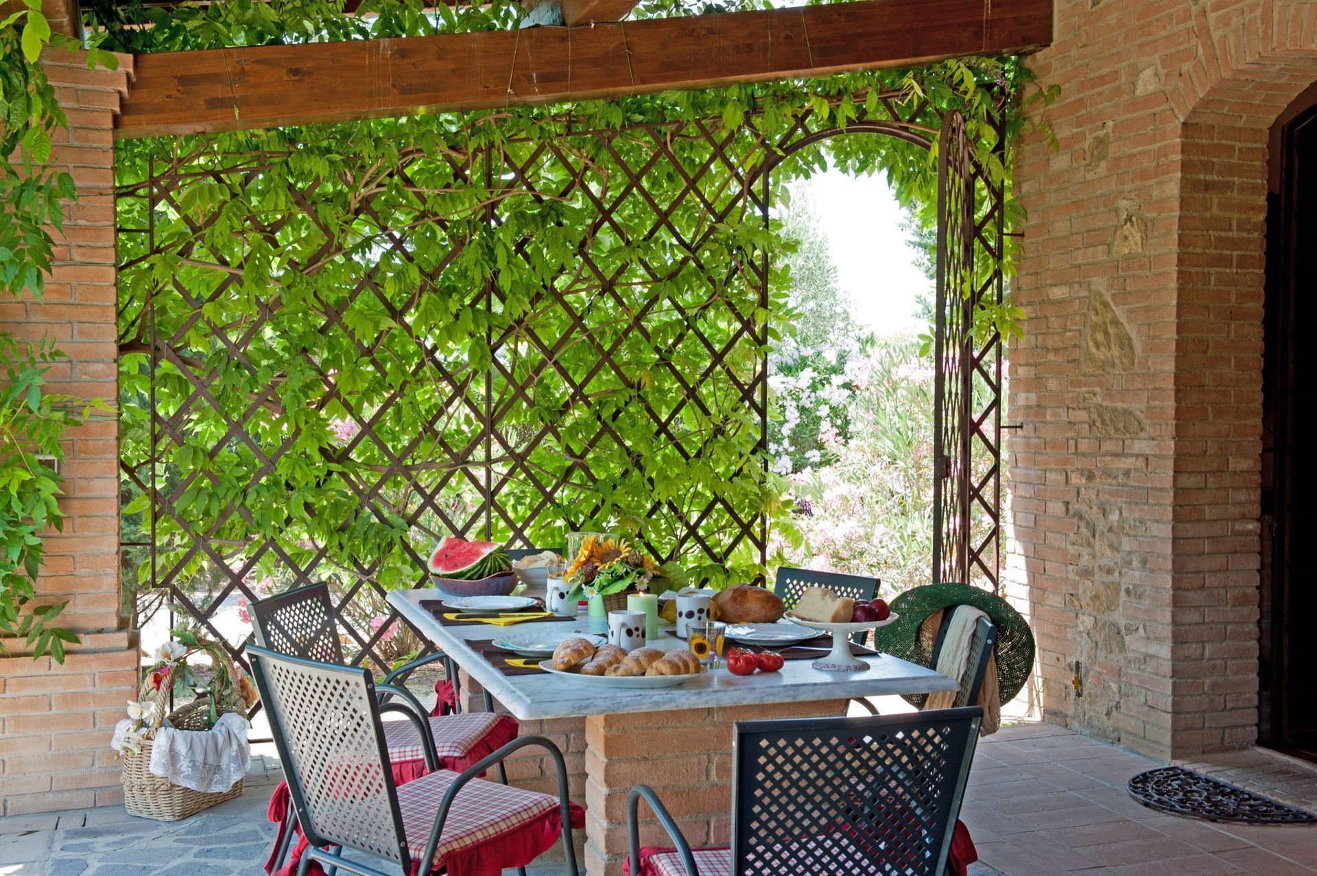 Een terras buiten met een tafel gedekt voor een maaltijd, omringd door stoelen en een houten pergola.