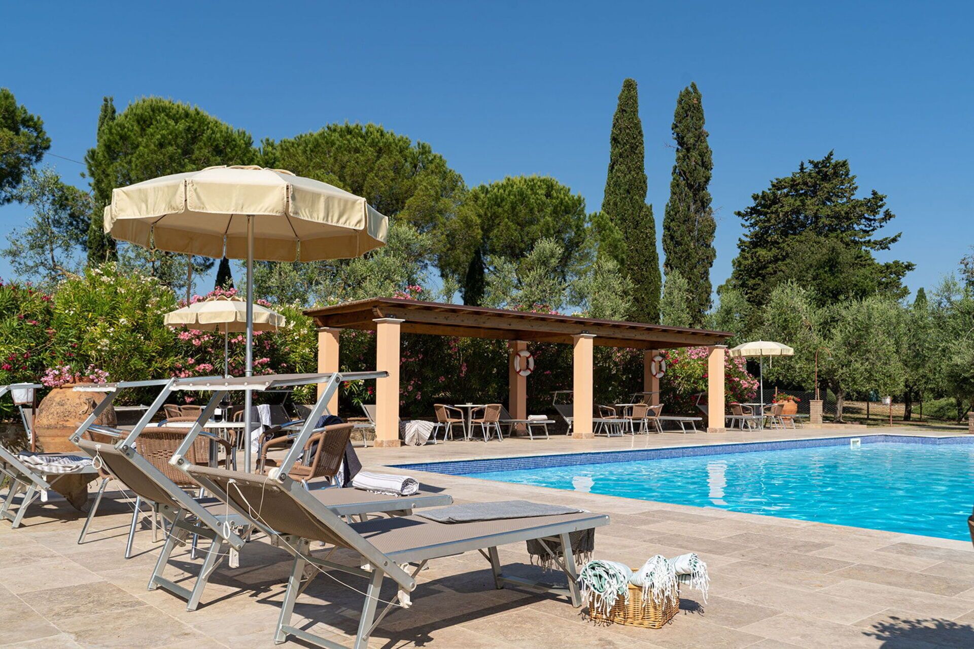 Zona de piscina con sillones, sombrillas y una pérgola.