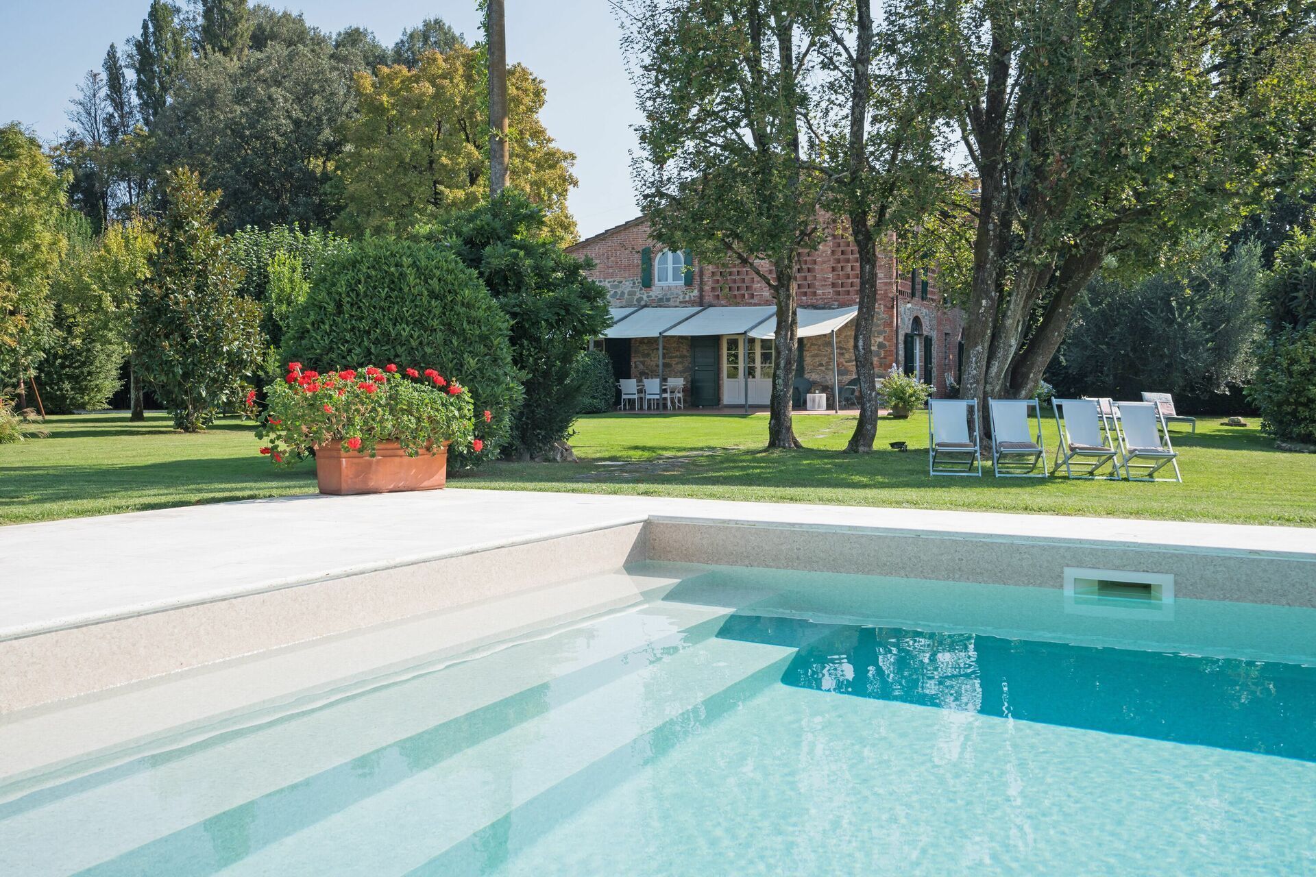 A swimming pool with a clear blue water, surrounded by a well-maintained lawn and a brick building in the background.