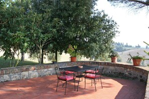 An outdoor patio with a table and chairs, surrounded by a stone wall and potted plants.