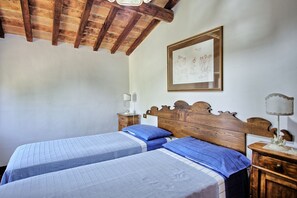 A bedroom with two beds, wooden headboards, a framed picture on the wall, a bedside table with a lamp, and a nightstand.
