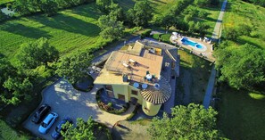Vista aérea de una propiedad con piscina, patio cubierto y zona de estacionamiento con varios coches.