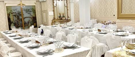 A banquet hall with long tables set for a formal event, featuring ornate columns and a large mirror.