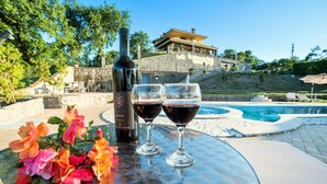 A bottle of wine and two glasses on a table by a poolside, with a stone wall and a building in the background. - I Gigli di Bolsena - Exclusive Villa Rental in Montefiascone, Lake Bolsena (Montefiascone)