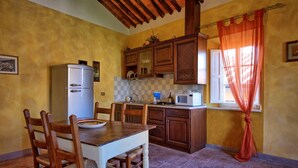 Una cocina con armarios de madera, un refrigerador blanco, un microondas y una mesa de comedor con sillas.