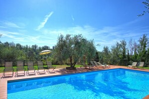 Una piscina con sillones de descanso y una sombrilla.