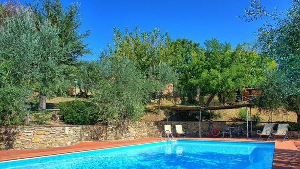 Una piscina con un muro de piedra y una pérgola con sillas.