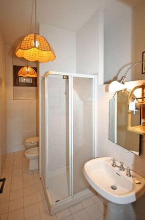 Un baño con ducha envuelta en vidrio, un lavabo blanco y una lámpara colgante.