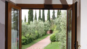 A room with a large window revealing a garden with trees and a path. - La Valle 3 - Apartment with pool (Montaione)