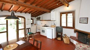 Una cocina rústica con suelo de baldosas, vigas de madera, horno empotrado y televisor.
