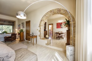 A spacious living room with a large window, a fireplace, and a dining area with a brick archway.