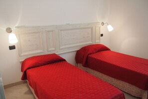 A room with two single beds, each with a red bedspread, and a white headboard with three panels.
