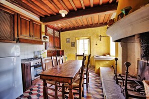 A traditional kitchen with wooden cabinets, a tiled backsplash, a dining table with chairs, and a fireplace.