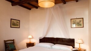 A bedroom with a bed, two bedside tables with lamps, a wooden headboard, and two framed pictures on the walls.