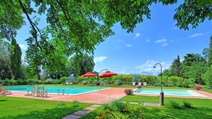 Ein Poolbereich mit zwei Schwimmbecken, roten Sonnenschirmen und einem Garten mit verschiedenen Pflanzen.