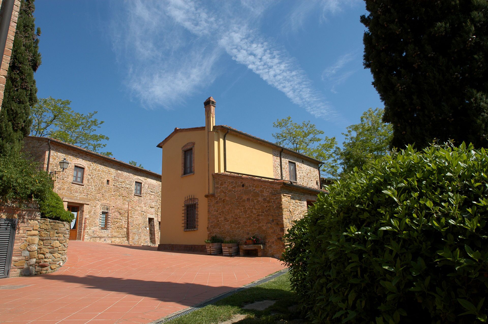 A traditional stone building with a yellow facade, a tiled courtyard, and a clear blue sky.