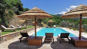 Zona de piscina con sillones de descanso, sombrillas y un muro de piedra.