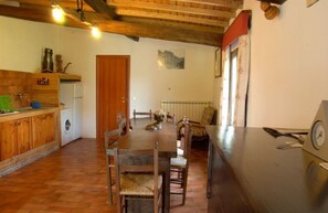 A rustic kitchen with wooden cabinets, a washing machine, and a dining area with a wooden table and chairs.