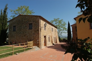 A stone building with a tiled courtyard, a wooden fence, and a view of the countryside.