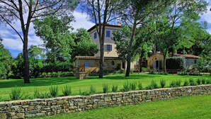 Una casa de piedra con un muro de piedra al frente, rodeada de césped verde y árboles.